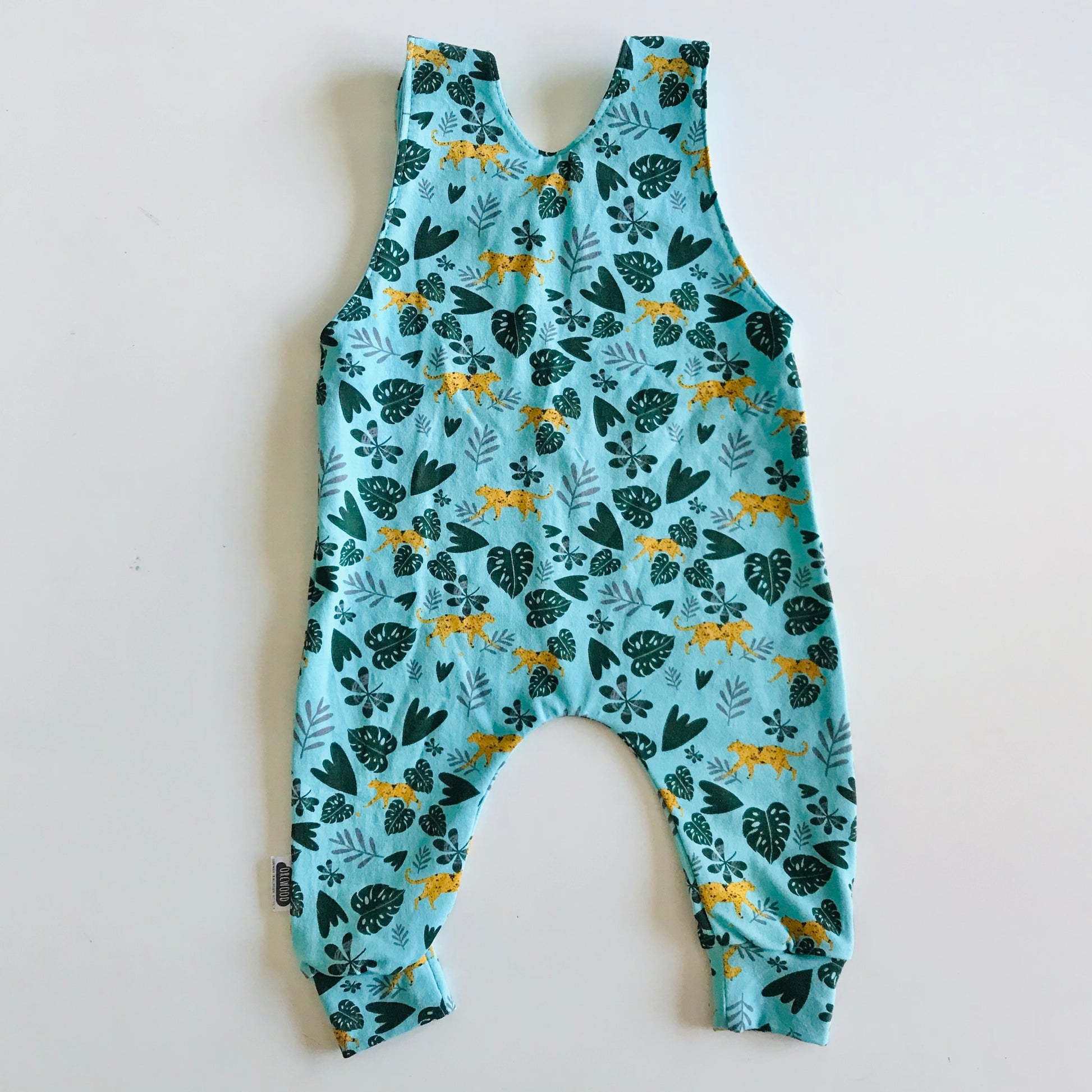 Children's long romper overalls with a cheetah and jungle leaves print on light blue background