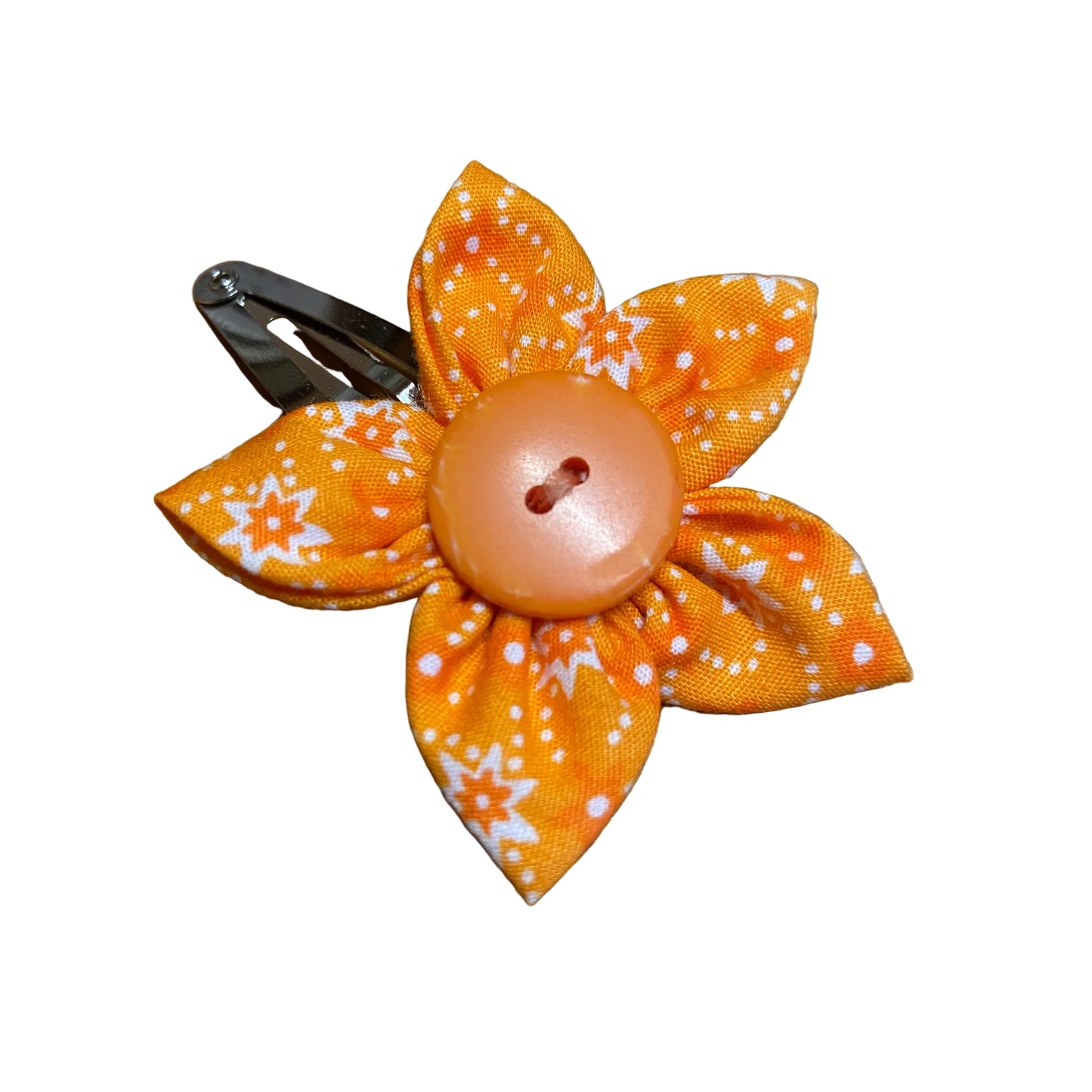 Orange flower-shaped hair clip with a button center on a wooden surface