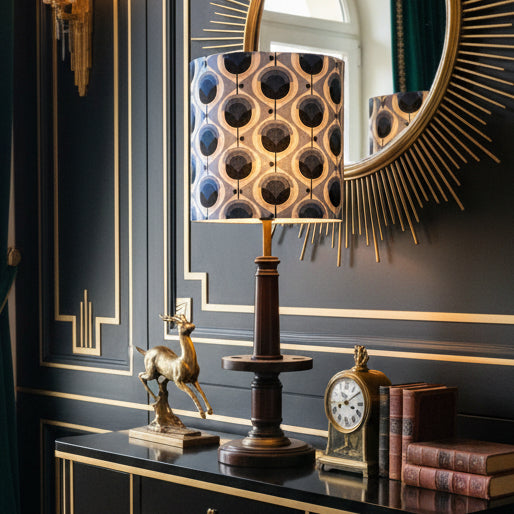 A table lamp with a cylindrical drum shade featuring a blue, white, and navy geometric pattern, mounted on a dark brown wooden pedestal base.