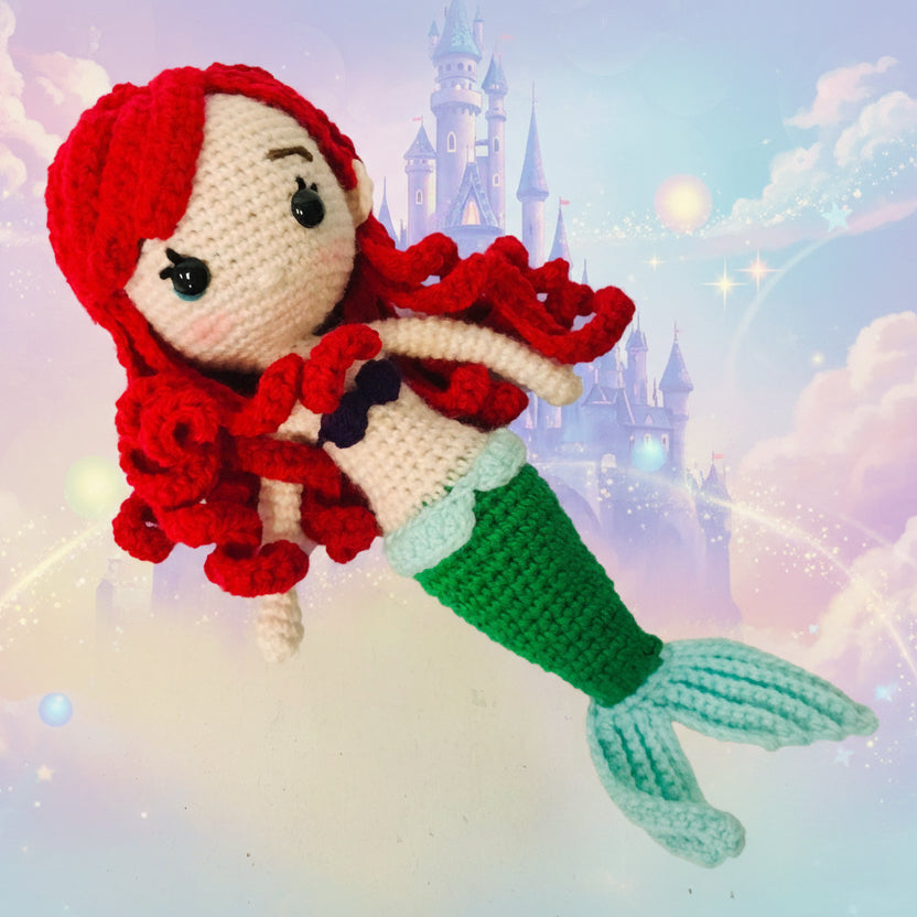 Crocheted mermaid toy with red hair and green tail on a white background