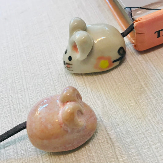 Two ceramic mouse-shaped bookmarks on a textured surface