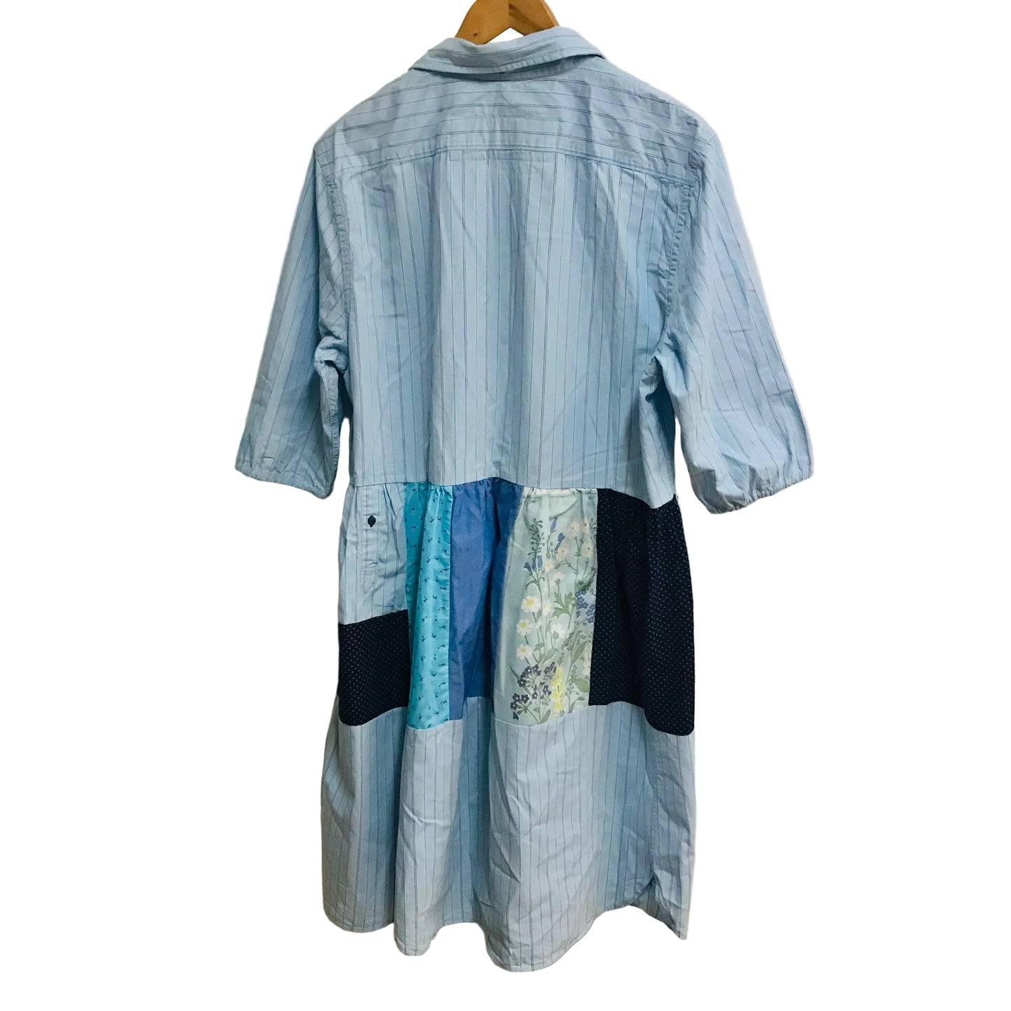 Blue patchwork dress on a hanger against a white wall