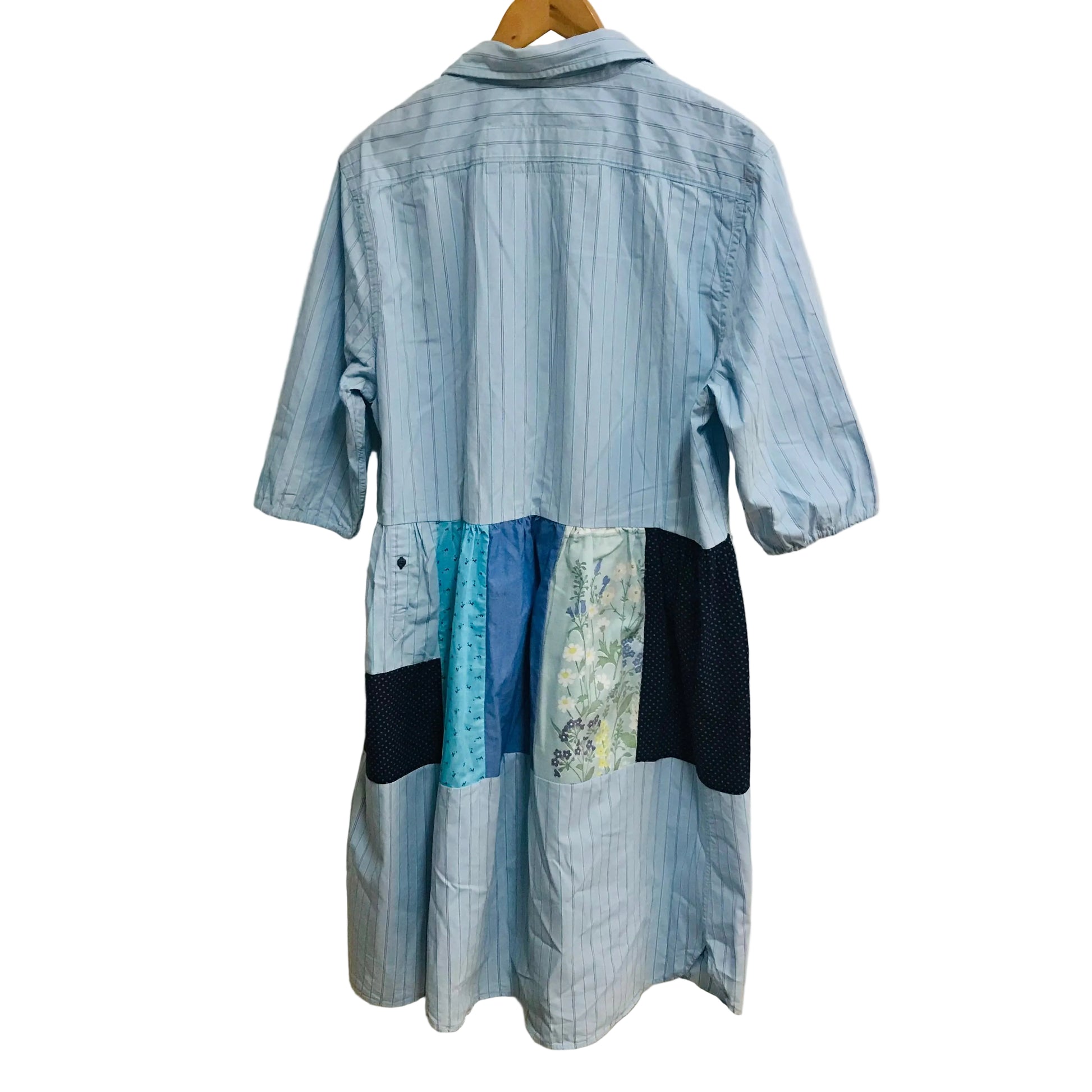 Blue patchwork dress on a hanger against a white wall