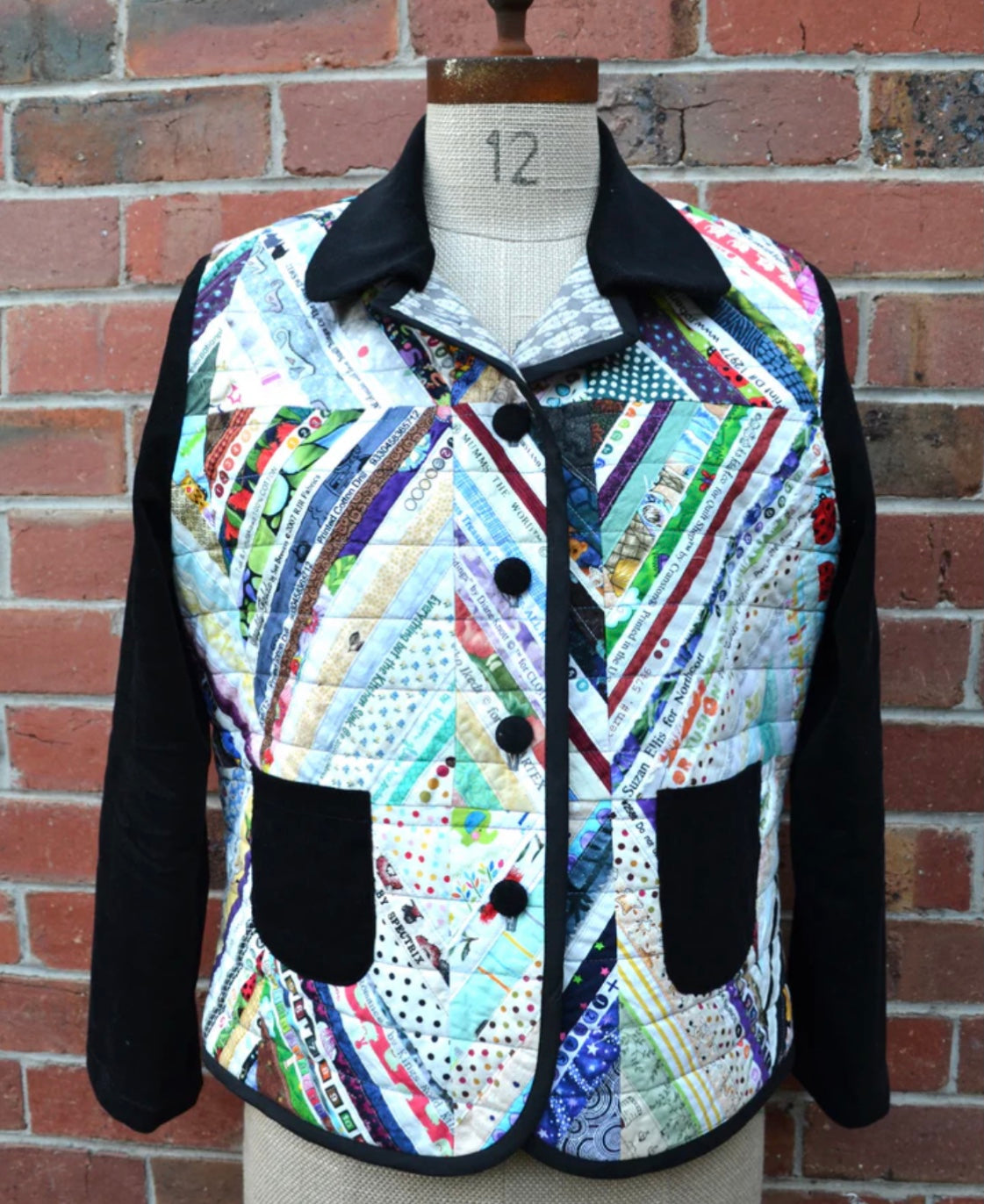 Colorful quilted jacket on a mannequin against a brick wall.