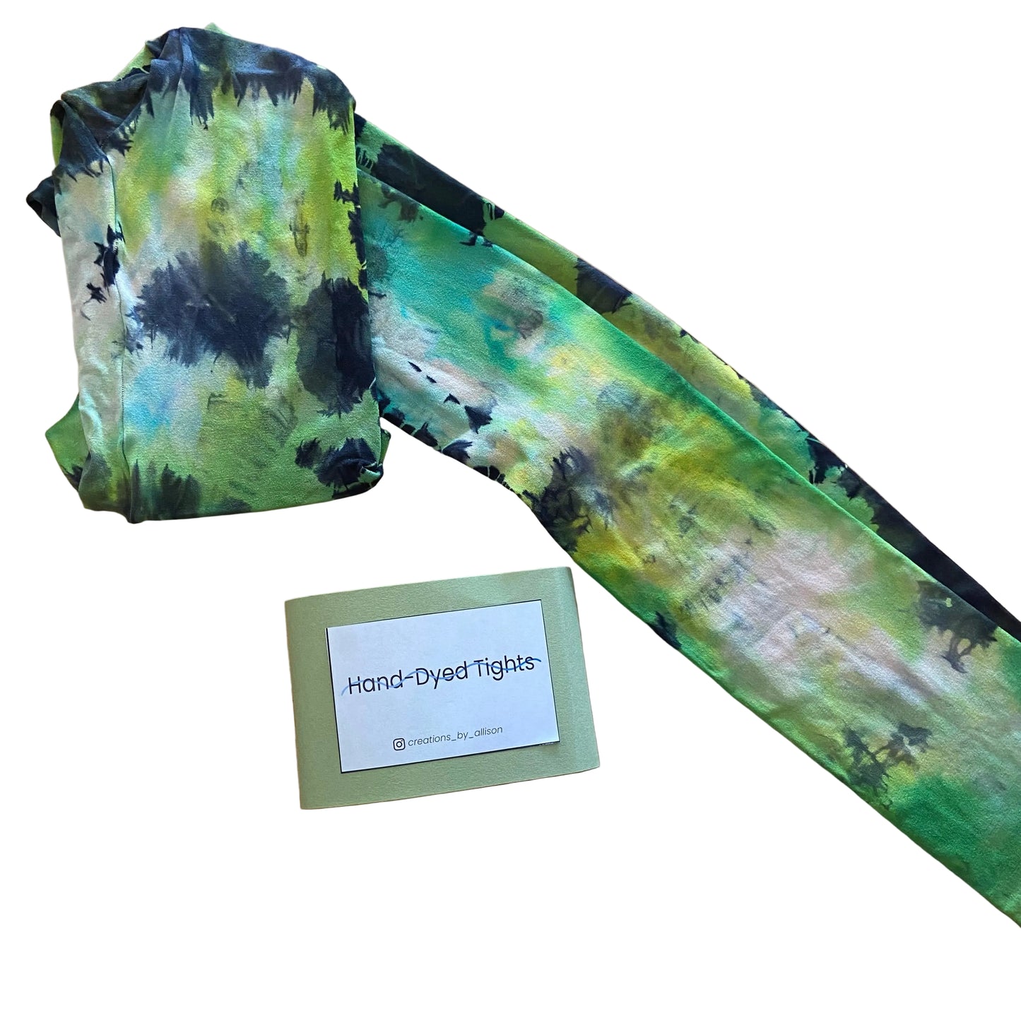 Hand-dyed tights with green and black pattern on a wooden surface, accompanied by a label.
