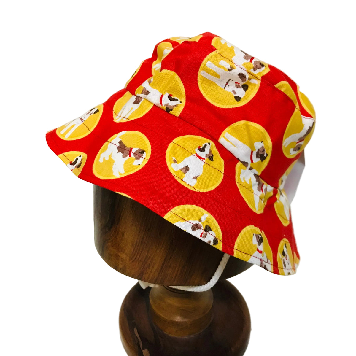 A red bucket hat with a yellow and white dog print, displayed on a wooden mannequin head against a plain white background.