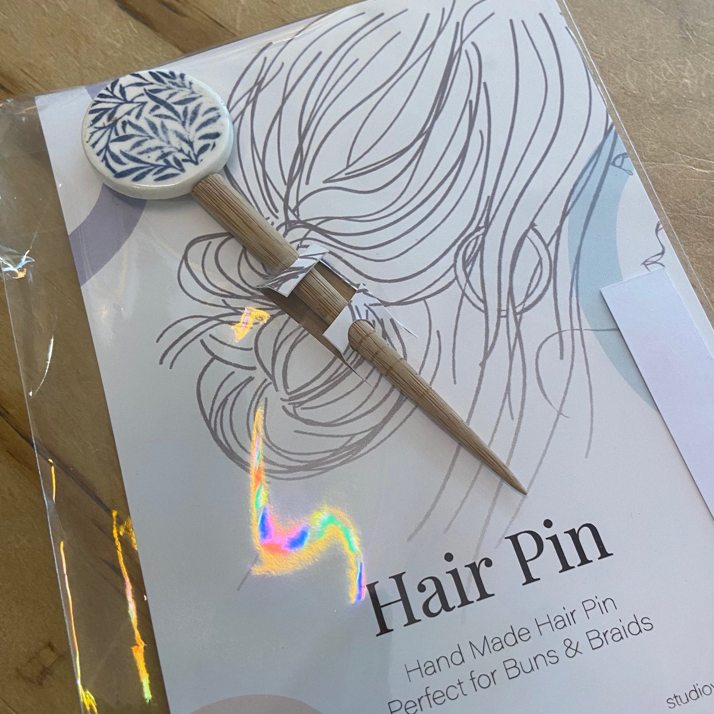Hair pin with packaging featuring a design of hair and text on a wooden surface