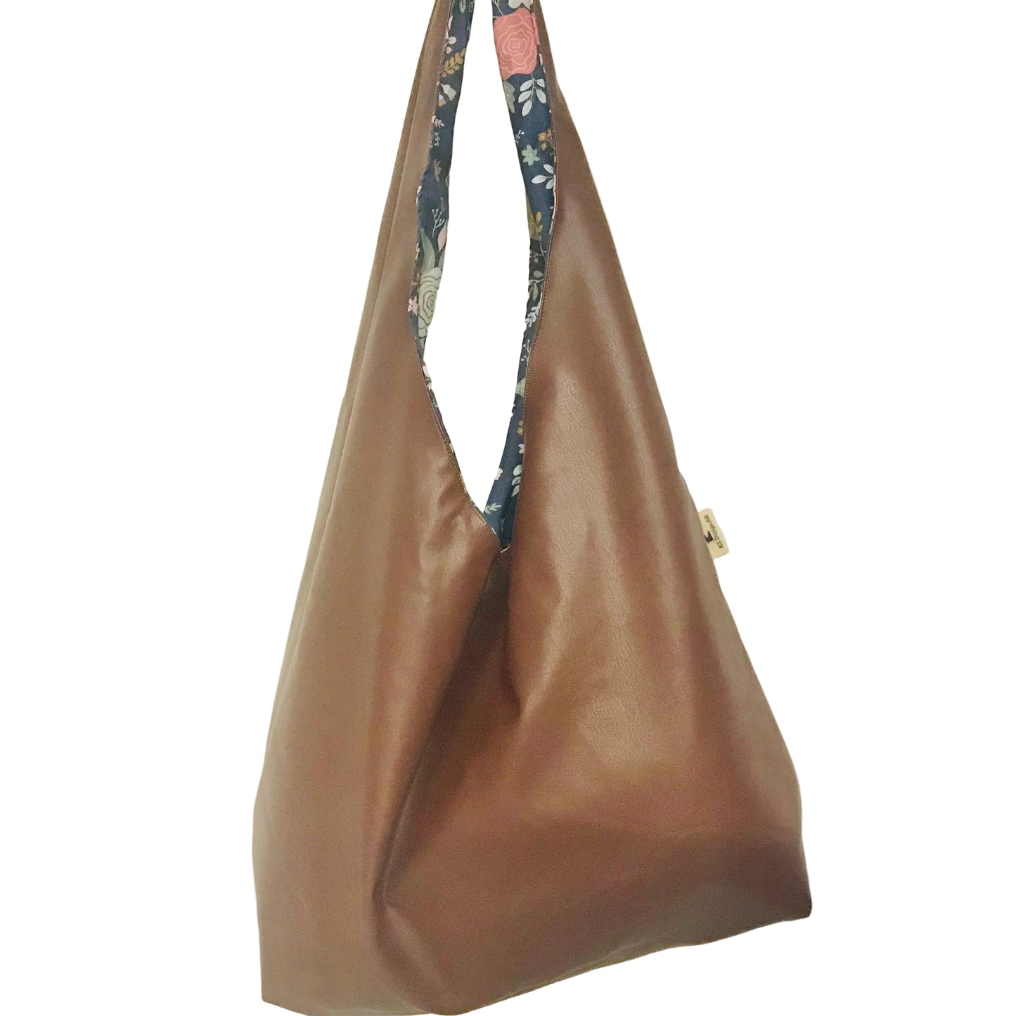 A brown faux-leather hobo shoulder bag with a floral-patterned fabric strap, hanging against a plain off-white wall.