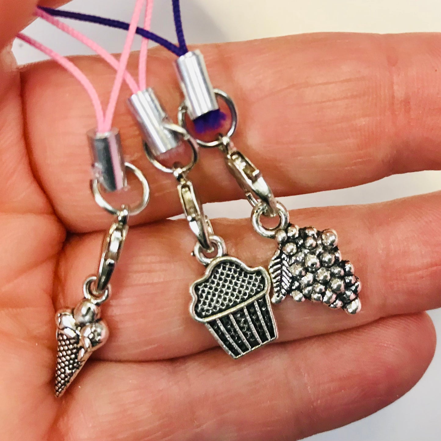 Three charms on strings held in a hand, including an ice cream cone, cupcake, and donut design.