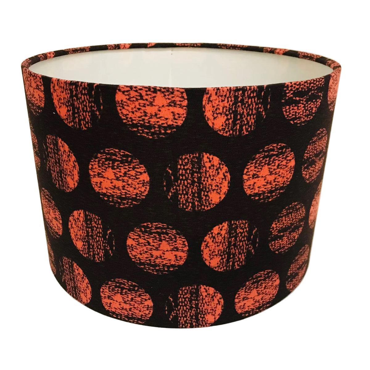 A cylindrical lampshade with a black background and a pattern of large orange-red textured polka dots, photographed against a plain off-white background.