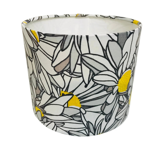 A fabric drum lampshade featuring a stylized floral line art pattern in black, white, gray, and bright yellow, photographed against a plain white background.