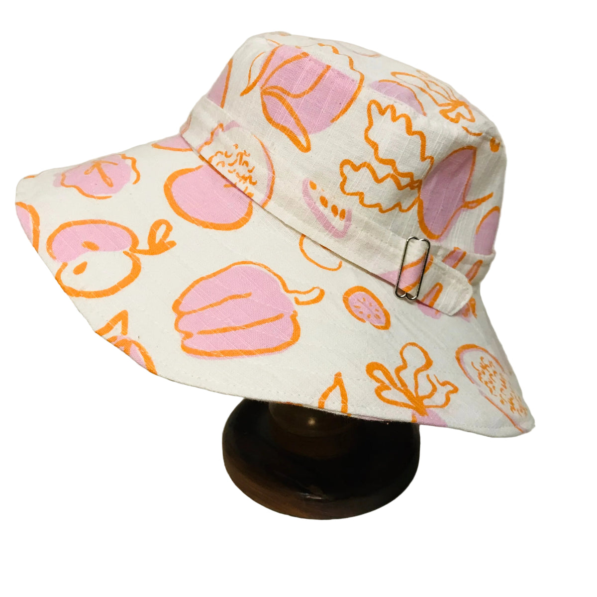 A white bucket hat with a pink and orange fruit pattern, displayed on a dark wooden stand against a plain white background.