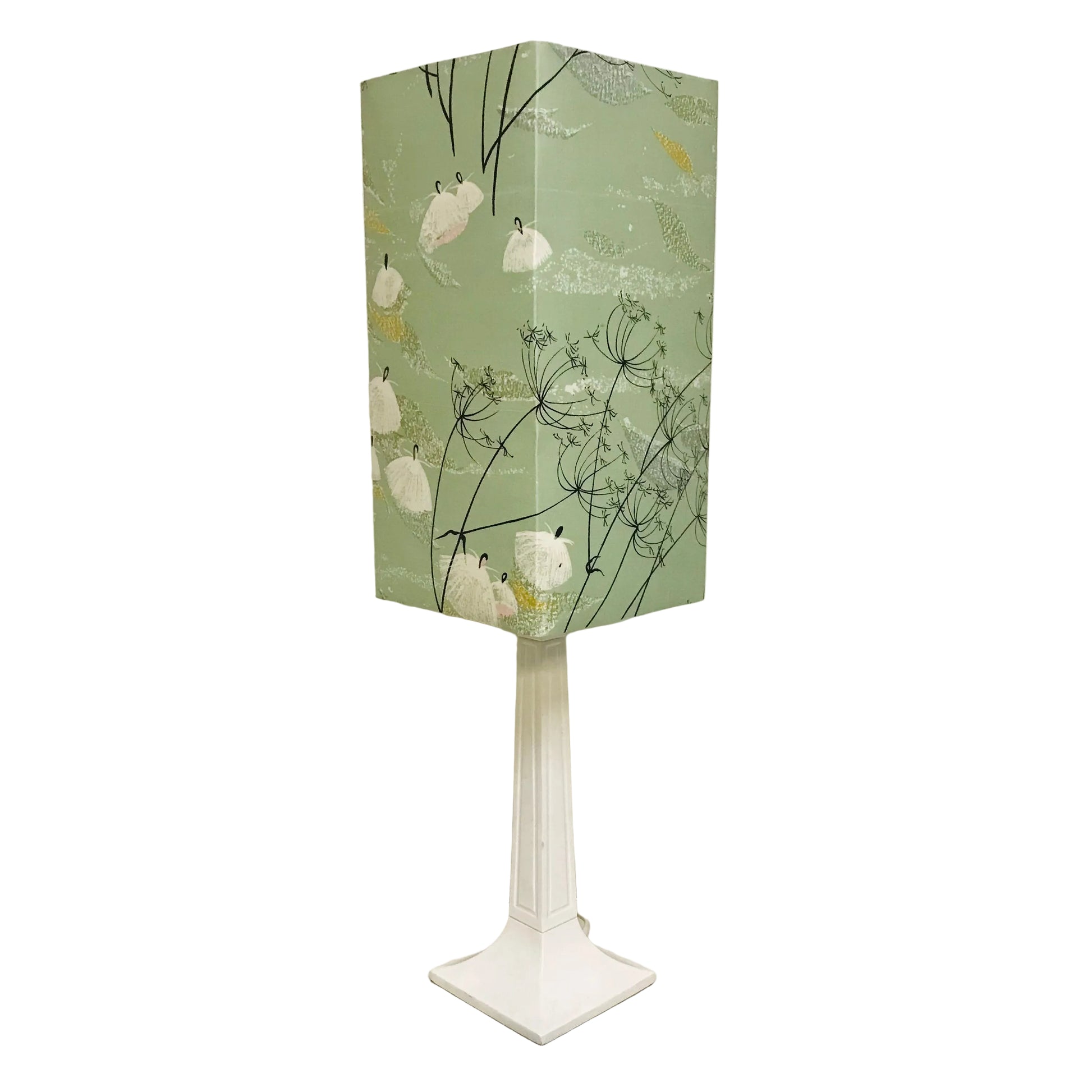 A modern table lamp with a tall, fluted white pedestal base and a hexagonal shade featuring a sage green background with a white and yellow wildflower pattern.