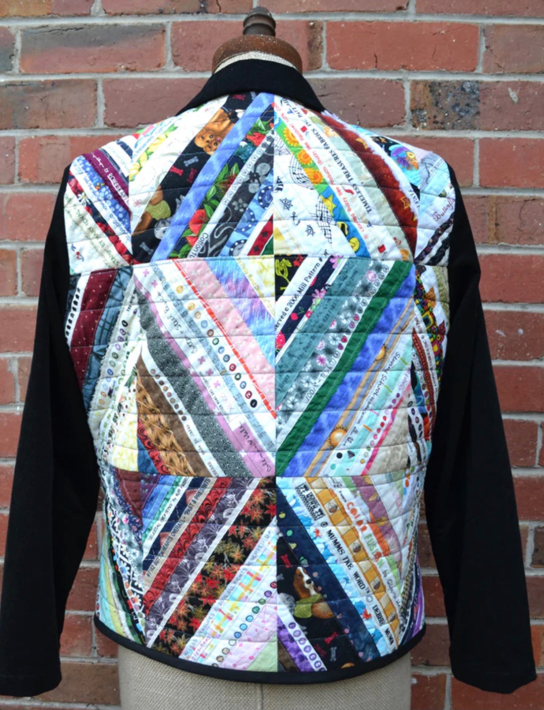 Colorful quilted jacket on a mannequin against a brick wall.