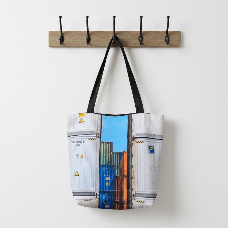 Tote bag with shipping container design hanging on a wooden hook rack.