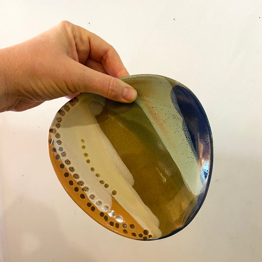 Hand holding a ceramic dish with a unique glaze pattern on a plain background