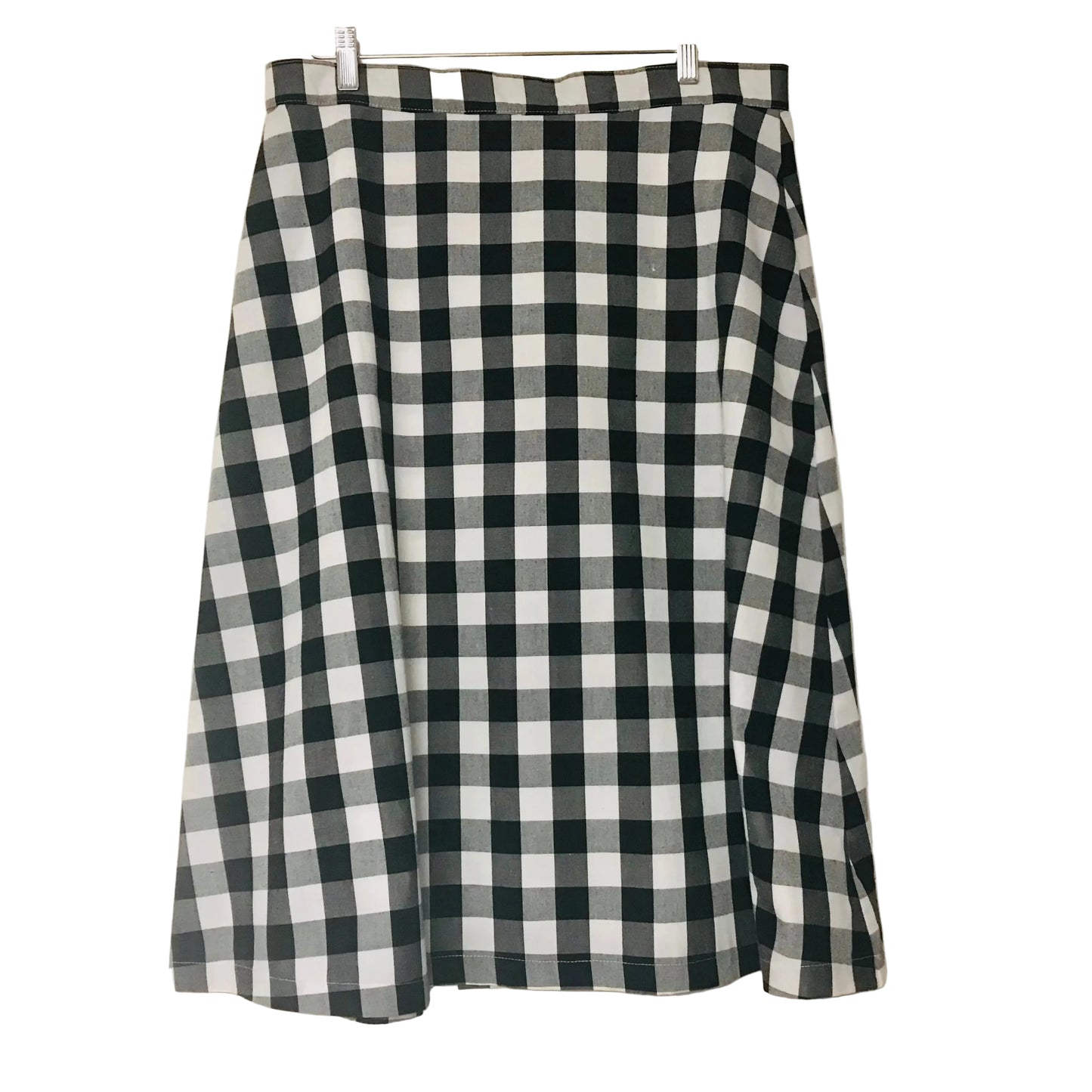 A black and white gingham checkered skirt hanging from a wooden hanger against a plain off-white wall.