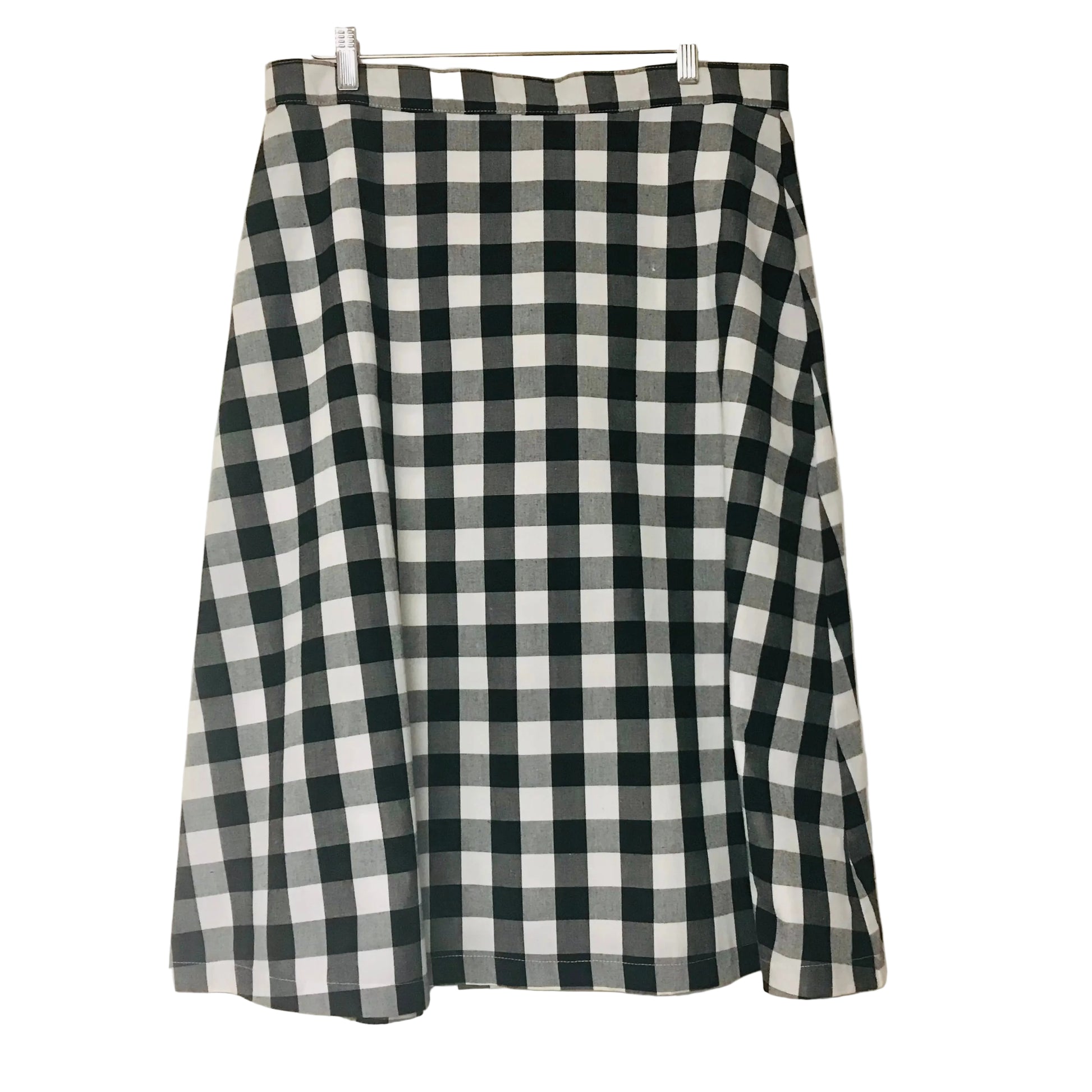 A black and white gingham checkered skirt hanging from a wooden hanger against a plain off-white wall.