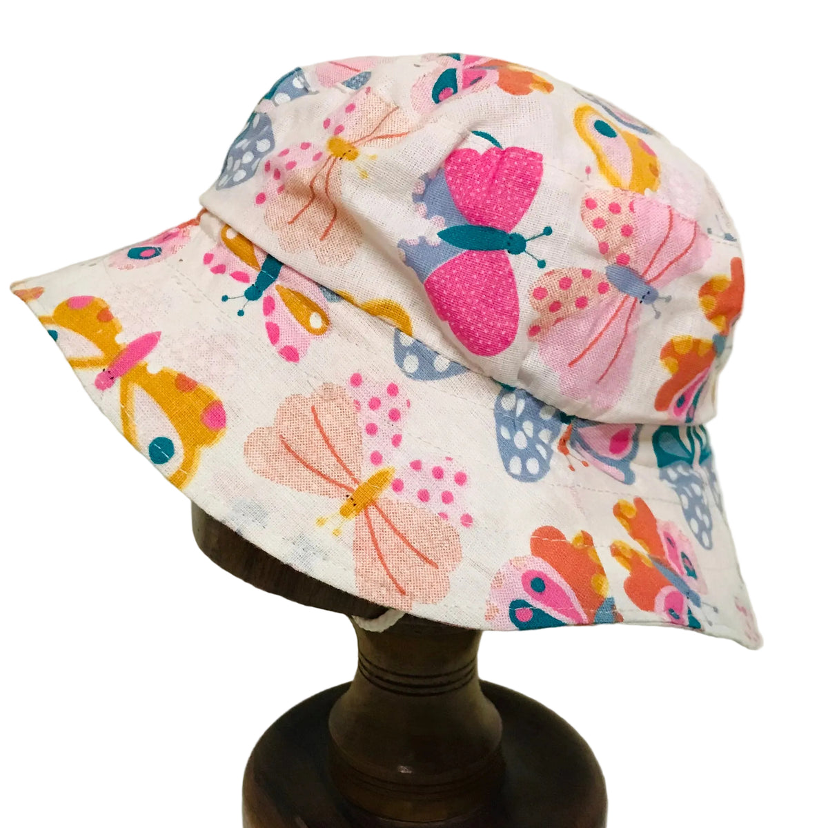 A white fabric bucket hat with a colorful butterfly print, displayed on a dark wooden stand against a plain off-white background.
