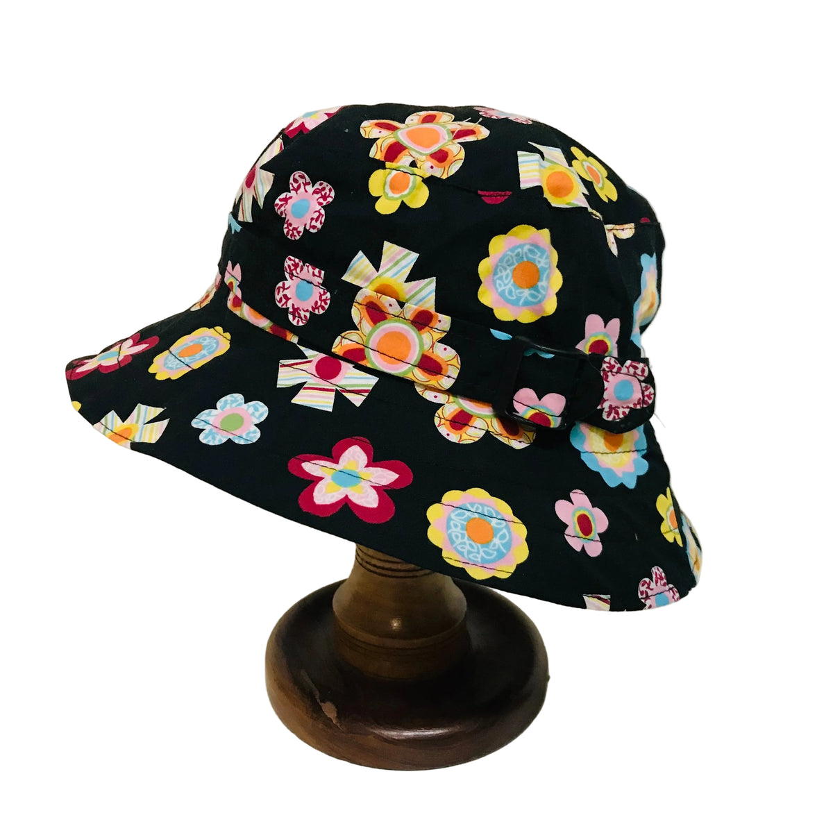 A black bucket hat with a colorful floral and bow pattern, displayed on a wooden stand against a plain white background.