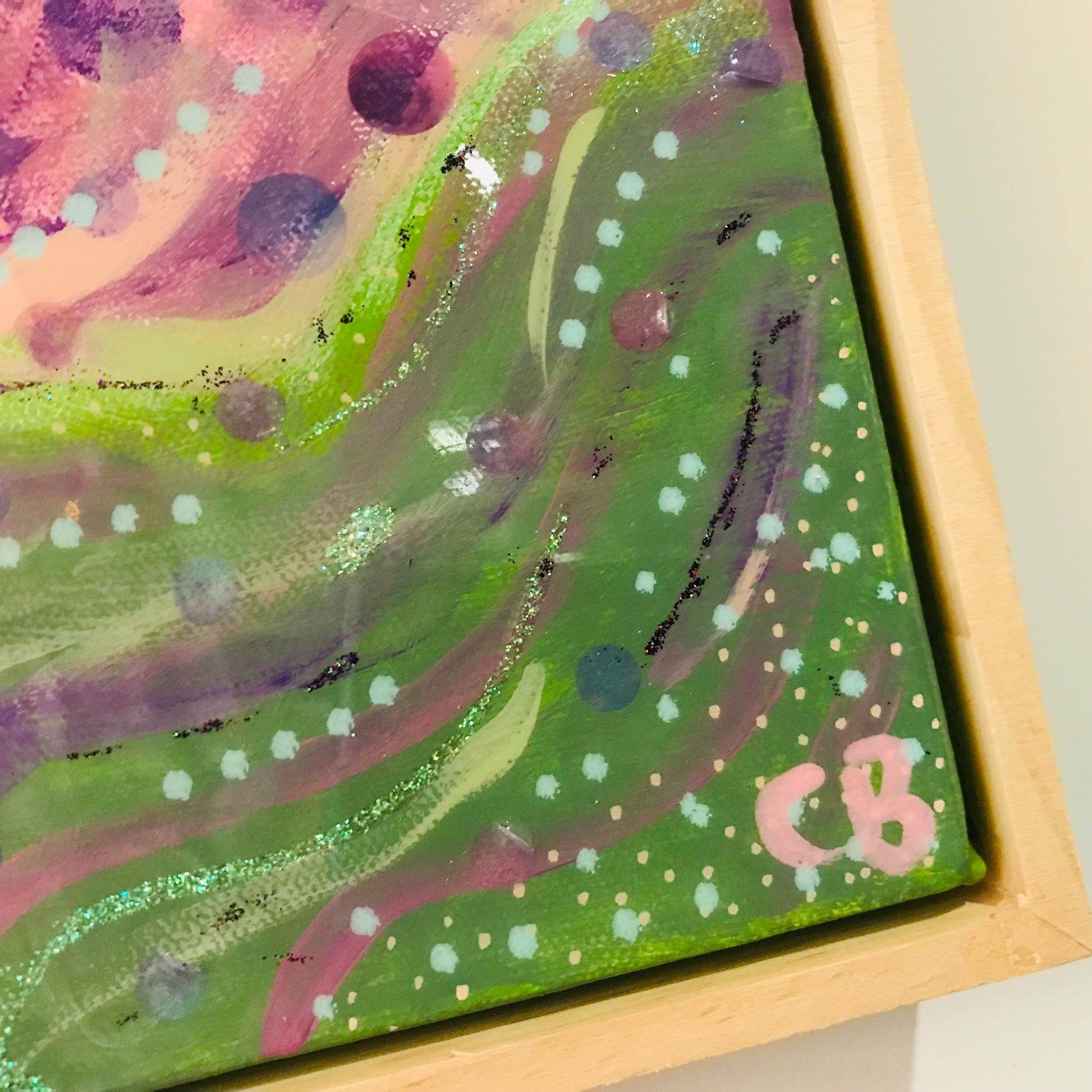 Abstract painting with swirling green, pink, and purple colors on a canvas with a wooden frame.
