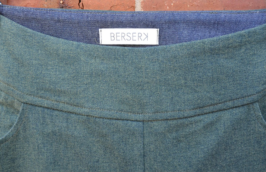 Close-up of a green garment with a Berserk label on a brick wall background
