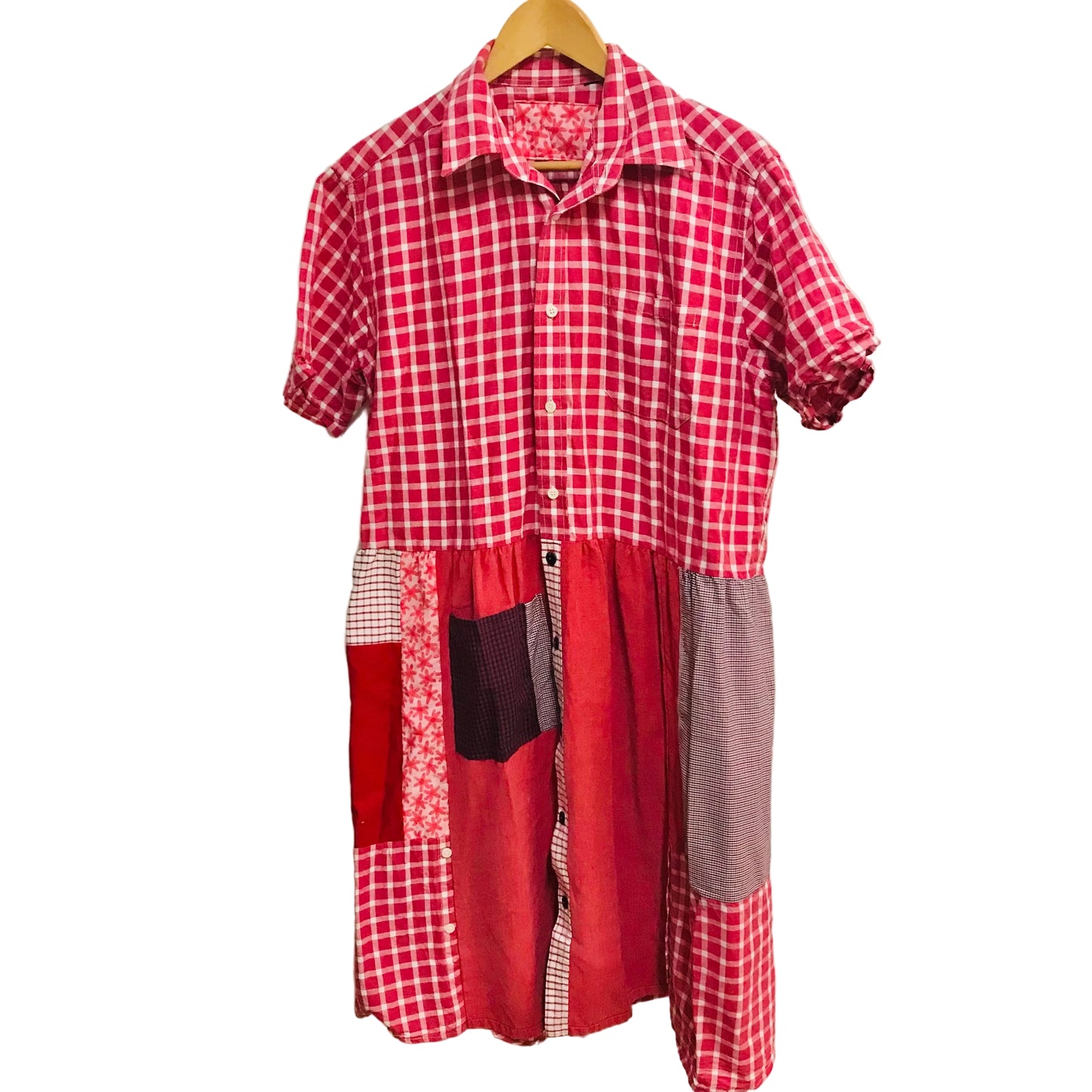 Red and white checkered dress with patchwork design on a hanger against a plain wall.