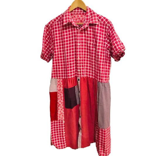 Red and white checkered dress with patchwork design on a hanger against a plain wall.