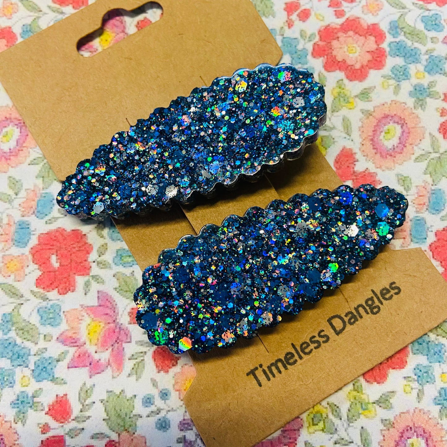 Blue glittery hair clips on a 'Timeless Dangles' card with a floral background