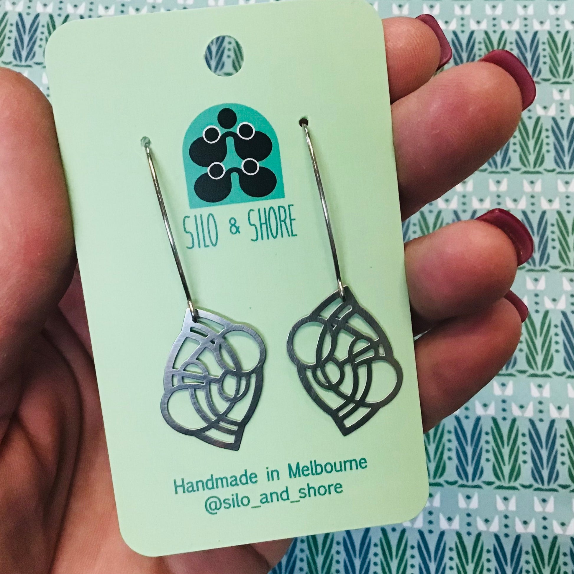 Silo & Shore earrings on a green card held by a hand with maroon nail polish.