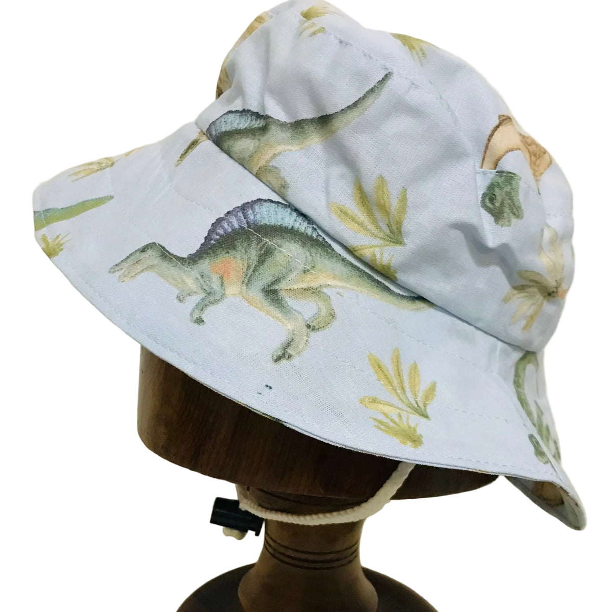 A light blue bucket hat with a dinosaur and fern pattern, displayed on a wooden mannequin stand against a plain off-white background.
