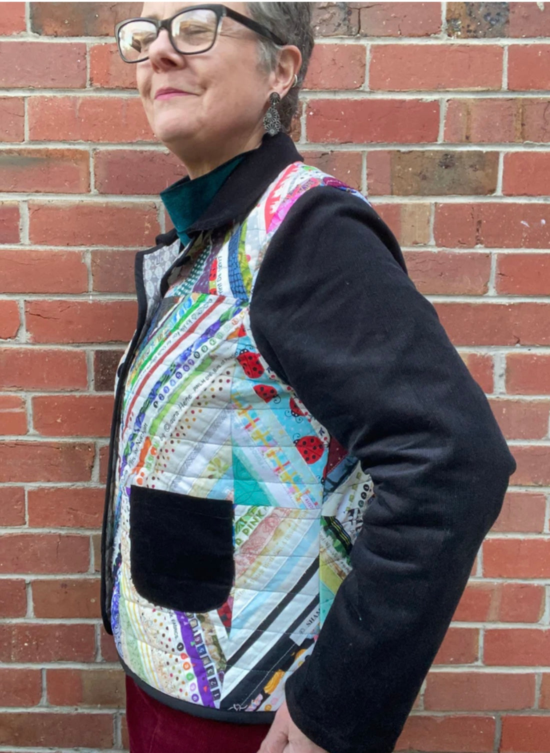 Person wearing a colorful quilted jacket against a brick wall