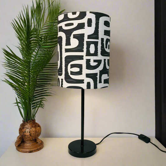Black and white patterned lamp with a plant on a white surface
