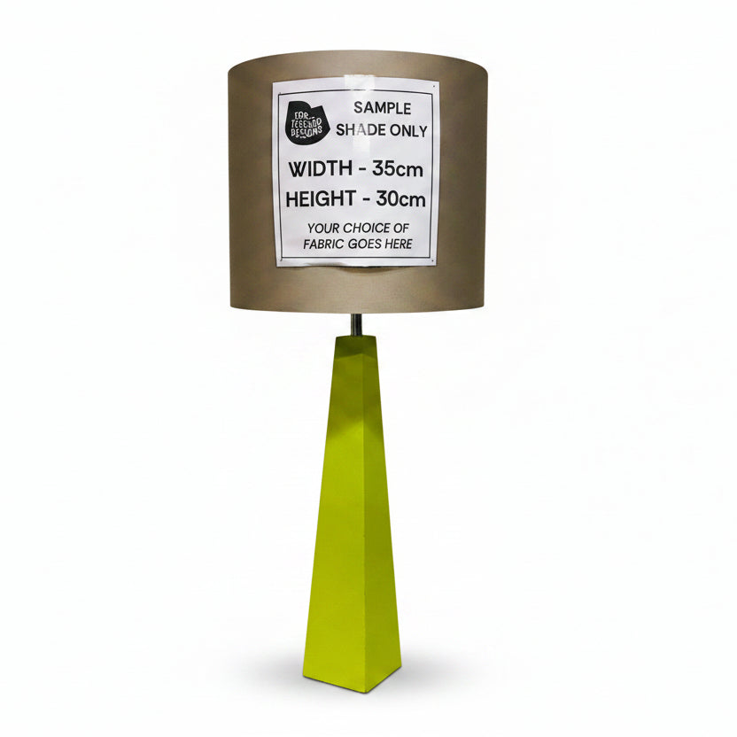 A custom fabric table lamp shade in a metallic taupe-brown color, mounted on a bright lime green geometric pedestal base. A white paper label is pinned to the front of the shade with dimensions and customization details.