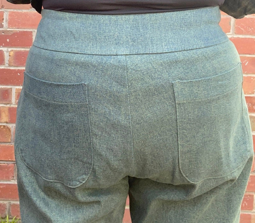 Green pants with two front pockets against a brick wall.