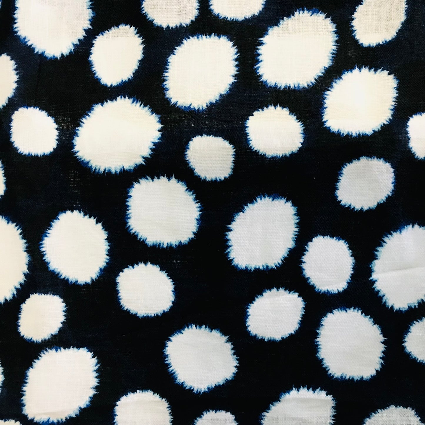 Pattern of blurred tye die white polka dots on a navy linen background