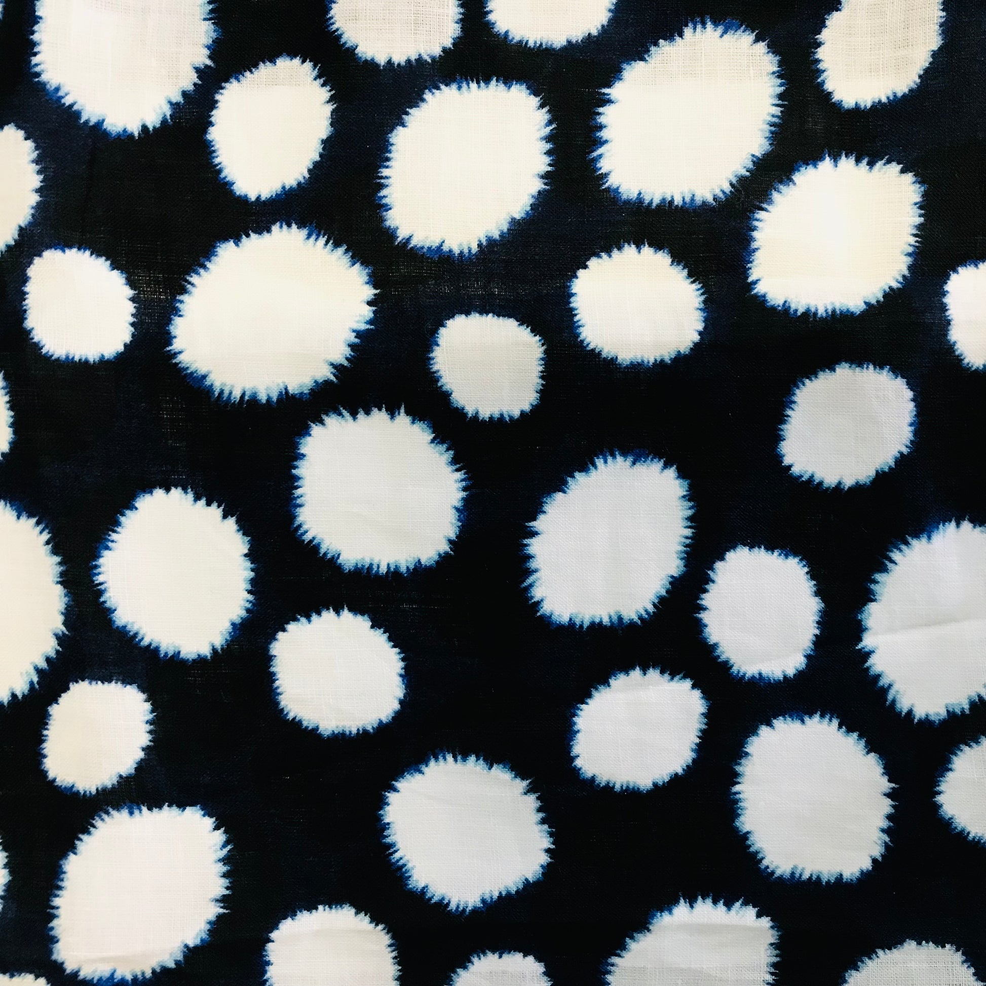 Pattern of blurred tye die white polka dots on a navy linen background