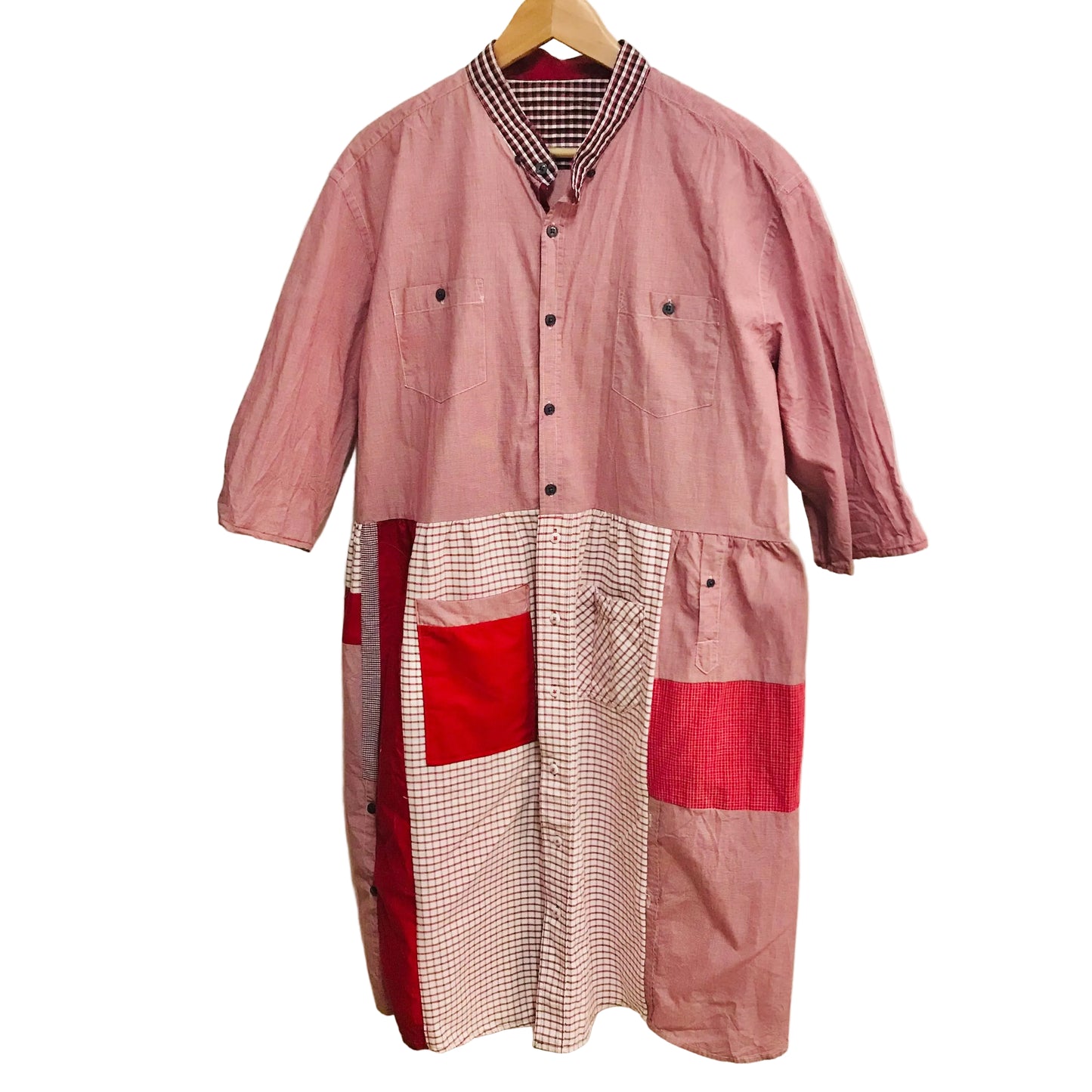 Patchwork dress with red and pink patterns on a hanger against a white wall.