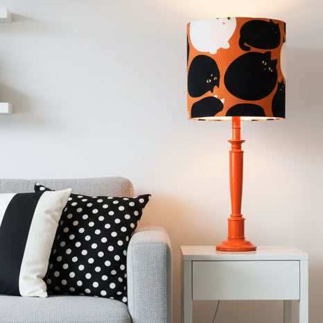 Table lamp with a black and white cat patterned shade on an orange base.