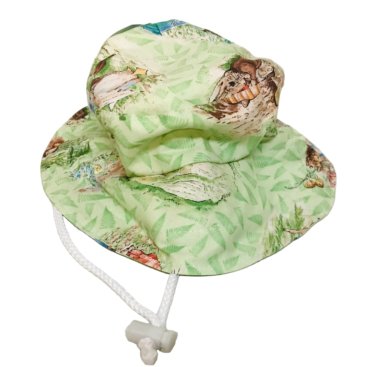 A light green sun hat with a tropical leaf and animal print, featuring a white drawstring closure, photographed on a light-colored floor against a plain wall.