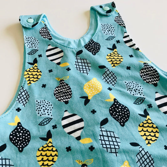 Children's sleeveless top detail of handmade long romper with lemon pattern on a light blue background