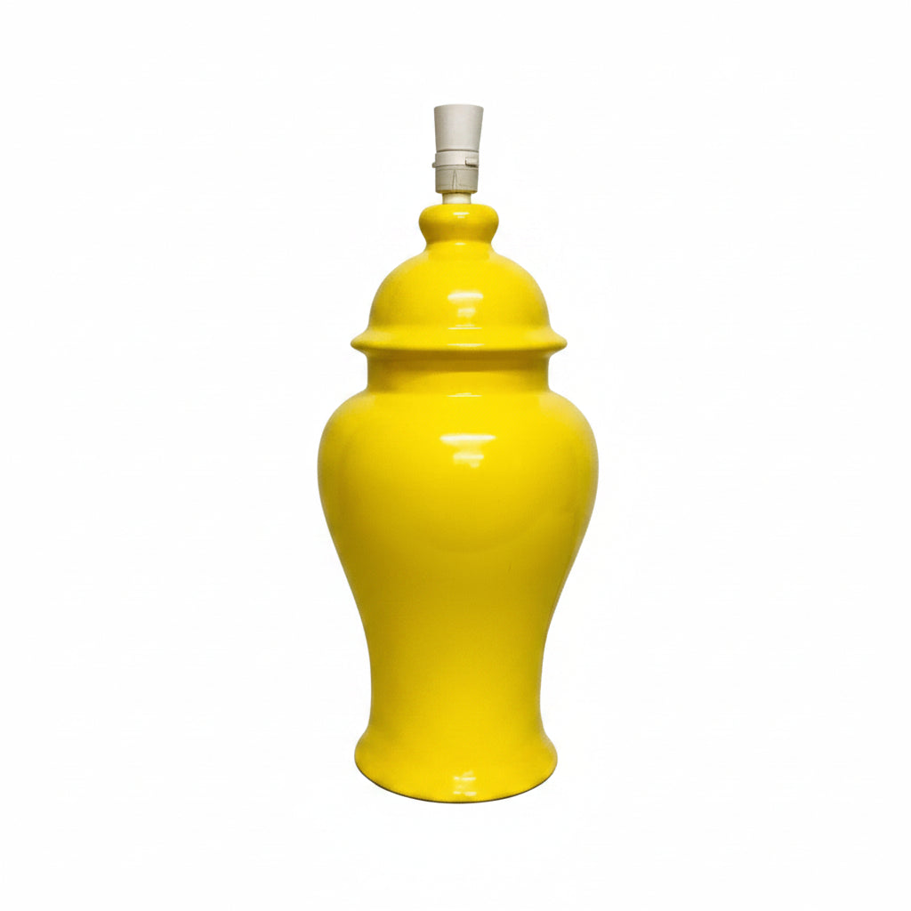 A bright yellow ceramic table lamp with a glossy finish and a white fabric lampshade, set against a plain off-white wall.