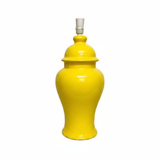A bright yellow ceramic table lamp with a glossy finish and a white fabric lampshade, set against a plain off-white wall.