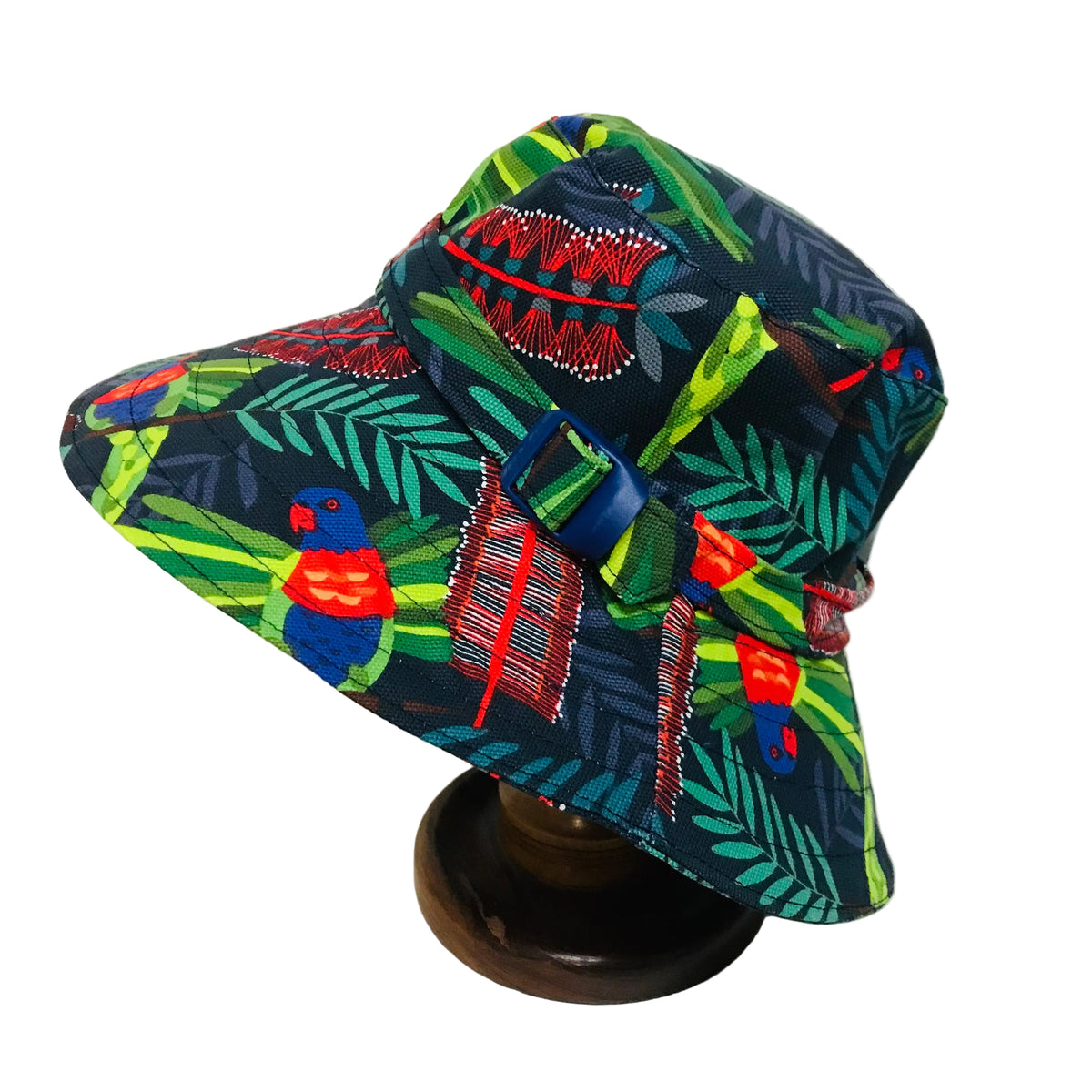 A wide-brimmed bucket hat with a vibrant tropical print featuring parrots, leaves, and geometric patterns, displayed on a wooden stand against a plain white background.