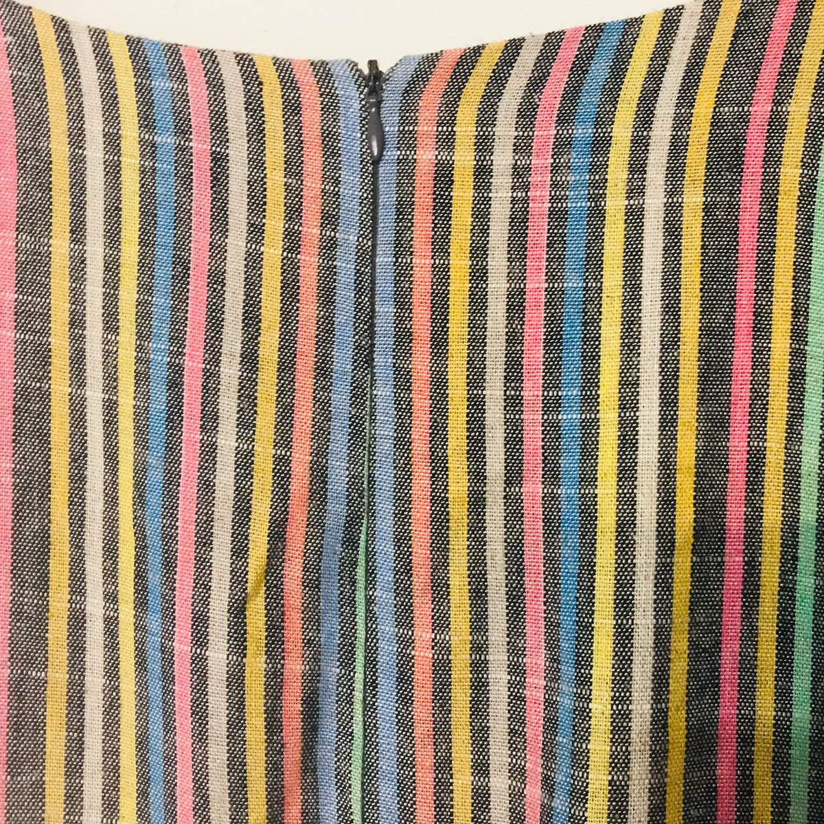Close-up of a striped textile with vertical multicolor lines including pink, yellow, blue, green, white, and dark gray/black, gathered at the center with a zipper.