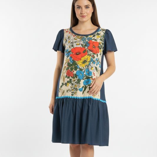 a model wearing a handmade dress with a dark navy blue base with a large, colorful floral print on the front panel and a light blue scalloped trim at the waist.