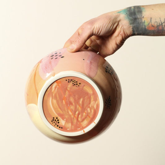 Hand holding a patterened ceramic bowl  on a beige background