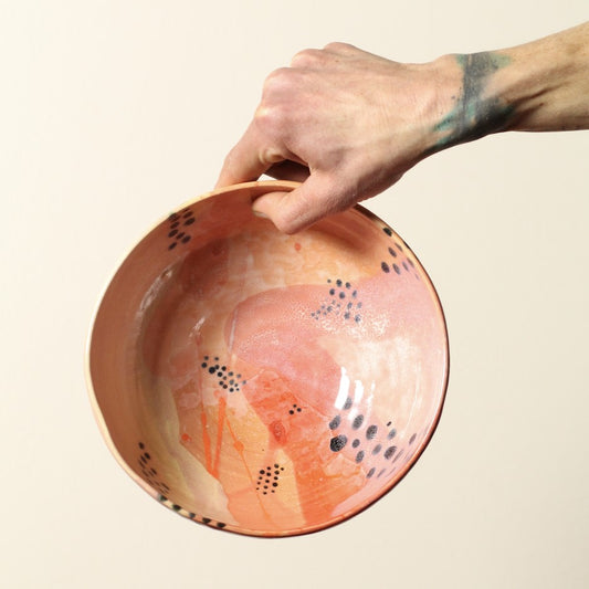 Hand holding a ceramic bowl with abstract design on a beige background