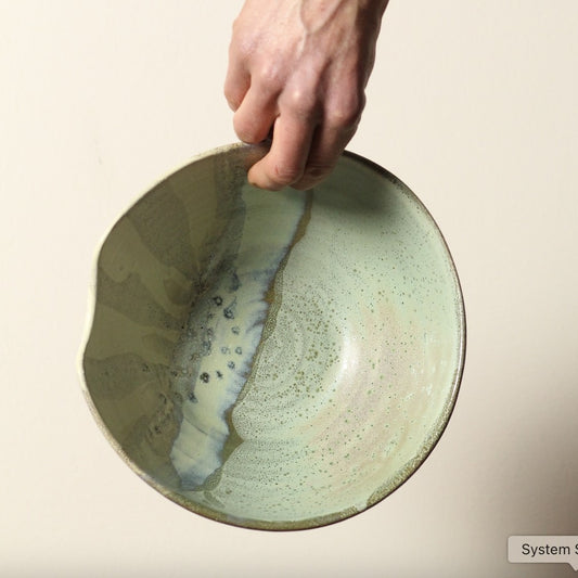 Hand holding a ceramic bowl with a marbled design on a beige background