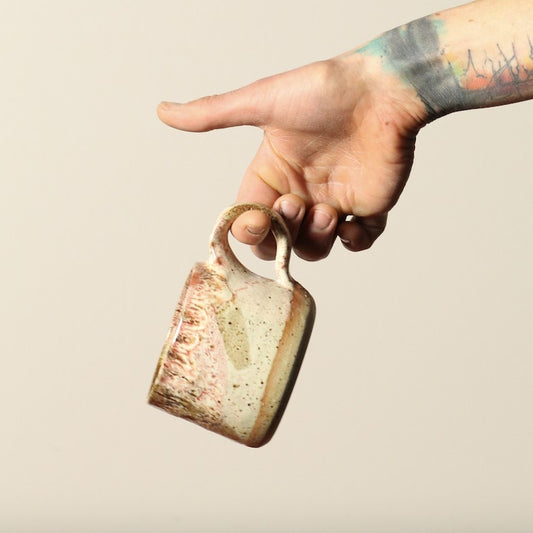 Hand holding a ceramic mug with a speckled design against a plain background